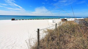Ein Strand mit weißem Sand, einem Holenzaun und blauem, klarem Himmel.