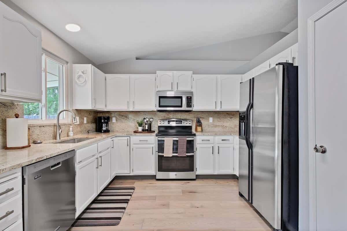 A modern kitchen with white cabinets, stainless steel appliances, and a wooden floor.