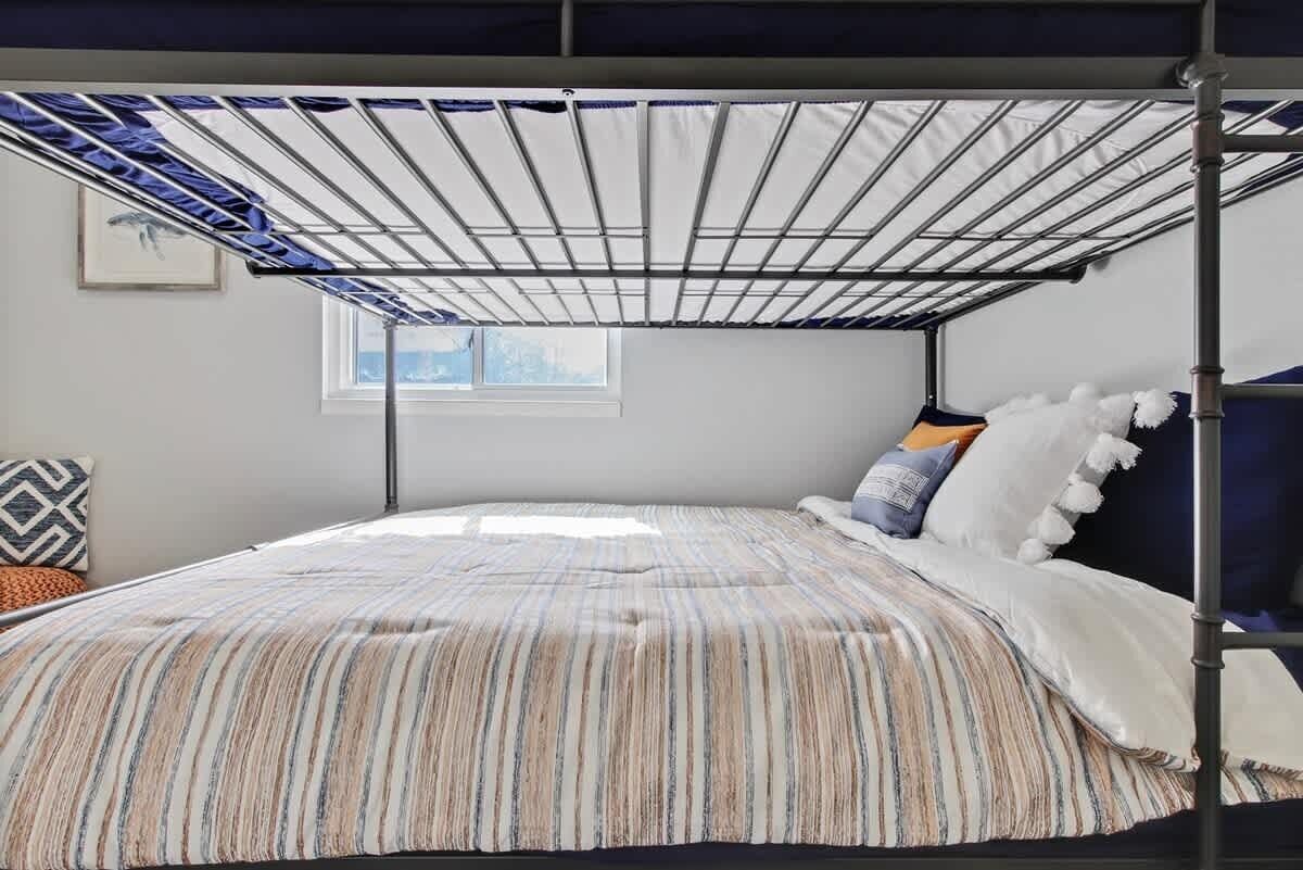 Una cama con colcha a rayas, una ventana y una estructura metálica sobre la cama.