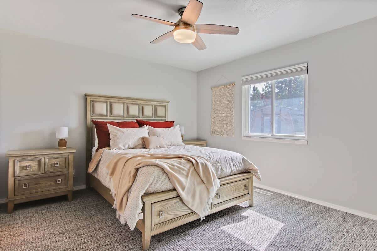 A bedroom with a bed, nightstand, lamp, ceiling fan, window, and a view of the outdoors.