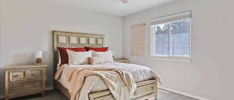A bedroom with a bed, nightstand, lamp, ceiling fan, window, and a view of the outdoors.