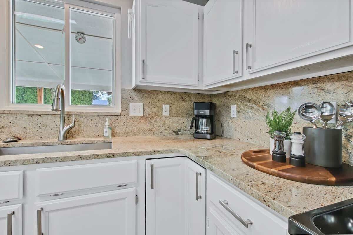 A kitchen with white cabinets, a granite countertop, a coffee maker, and a window.