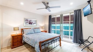 A bedroom with a bed, wooden nightstands, a ceiling fan, a TV, and a window with curtains.