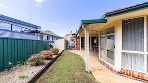 A residential property with a covered patio, a small garden with flowers, and a barbecue area.
