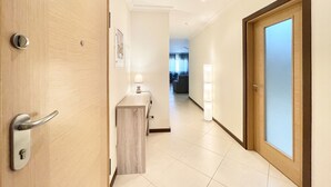 Un pasillo de hotel con una puerta de madera, un pequeño escritorio con una lámpara, y vistas a una sala de estar con sofá y cortinas.