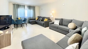 Una sala de estar moderna con un sofá seccional gris, un televisor de pantalla plana y un comedor con sillas azules.