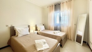 Habitación de hotel con dos camas, una mesita de noche con lámpara, una ventana con cortinas y un espejo.