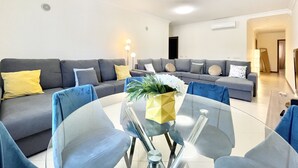 Una sala de estar moderna con una mesa de centro de vidrio, sofás grises y cojines amarillos.