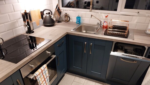 A modern kitchen with a black stove, blue cabinets, and a stainless steel sink. - Amy's Place Charming 3 Bed House Donegal (Stranorlar)