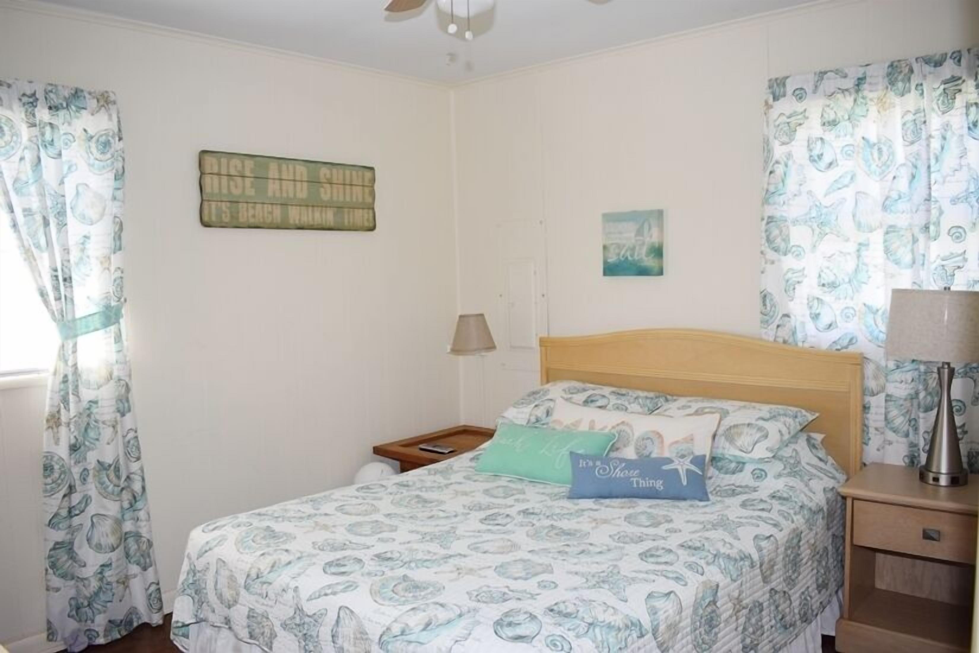A bedroom with a bed, a nightstand, a lamp, and a wall with a sign.