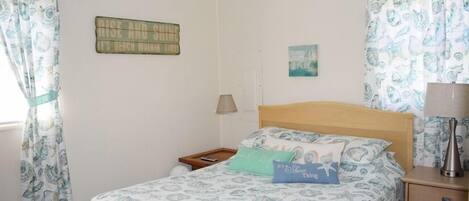 A bedroom with a bed, a nightstand, a lamp, and a wall with a sign.