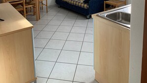 Een compacte kamer met een bank, een eettafel met stoelen, en een keukenhoek met een spoelbak.