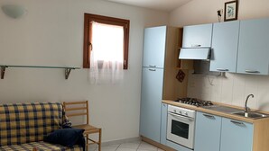 Een compacte keuken met een eethoek, met een gestreept bankje, houten stoelen, een tafel en lichtblauwe keukenkastjes.