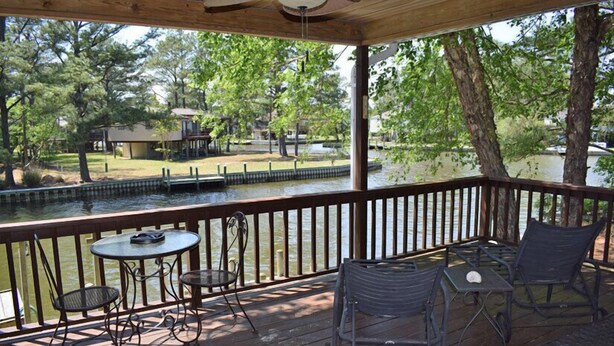 A covered outdoor deck with tables and chairs, overlooking a body of water and a park area. - Horsin Around | 3BR with Private Dock, Deck and Pet-Friendly (Chincoteague)
