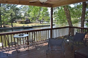 A covered outdoor deck with tables and chairs, overlooking a body of water and a park area. - Horsin Around | 3BR with Private Dock, Deck and Pet-Friendly (Chincoteague)
