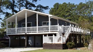 A two-story house with a balcony, a covered front porch, and a wooden deck. - Horsin Around | 3BR with Private Dock, Deck and Pet-Friendly (Chincoteague)