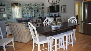 A dining area with a dark wooden table, white chairs, and a chandelier. - Horsin Around | 3BR with Private Dock, Deck and Pet-Friendly (Chincoteague)