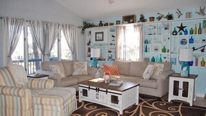 A living room with striped armchairs, a sofa, a coffee table, and a bookshelf filled with decorative items. - Horsin Around | 3BR with Private Dock, Deck and Pet-Friendly (Chincoteague)
