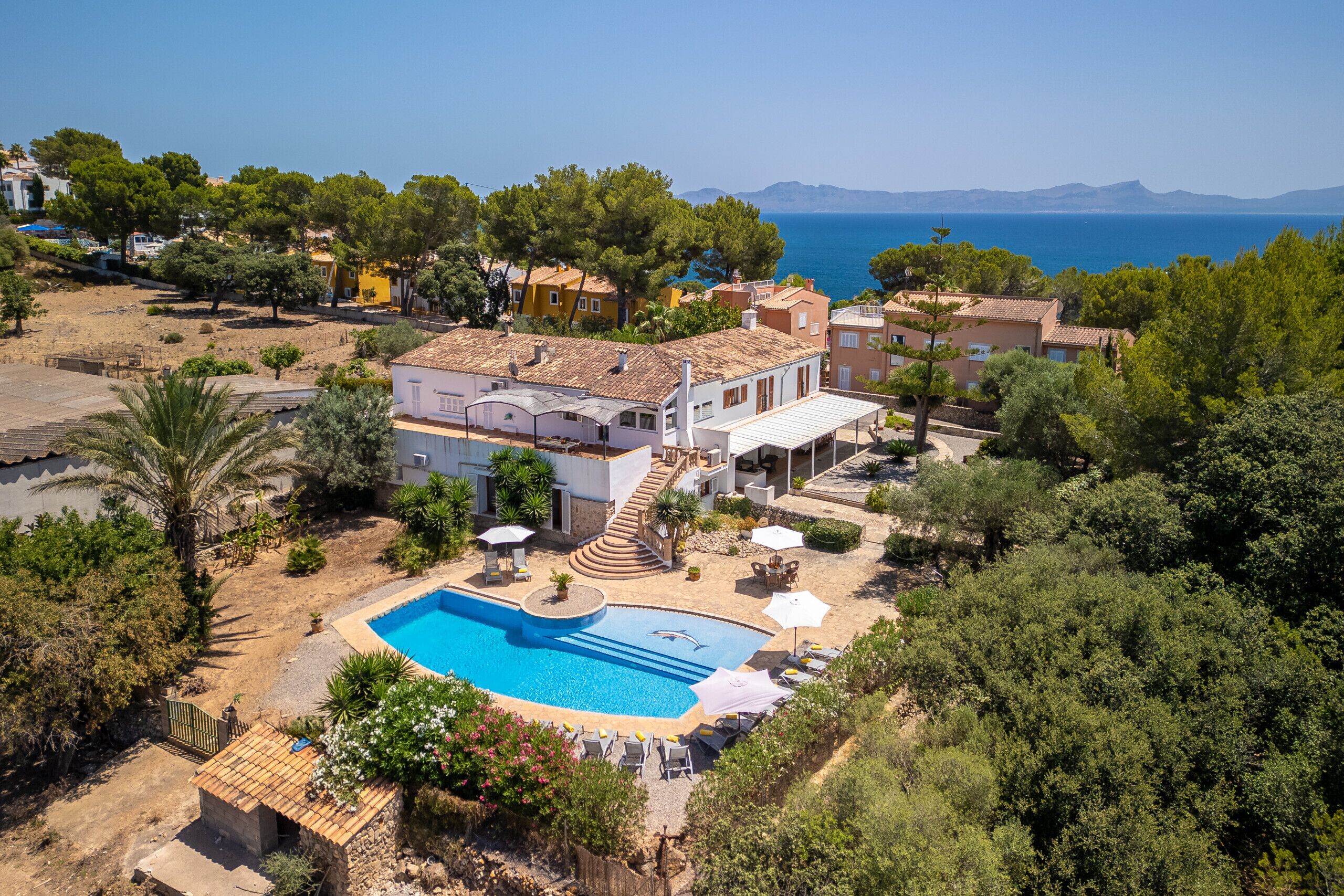 Eine Villa im mediterranen Stil mit Swimmingpool, umgeben von üppiger Vegetation und mit Blick auf das Meer.