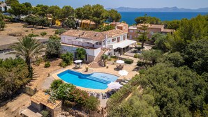 Une villa de style méditerranéen dotée d’une piscine, entourée d’une végétation luxuriante et offrant une vue sur la mer.