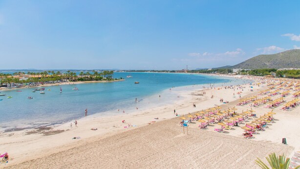 Une plage à l’eau d’un bleu limpide, avec un rivage sablonneux et de nombreux parasols.