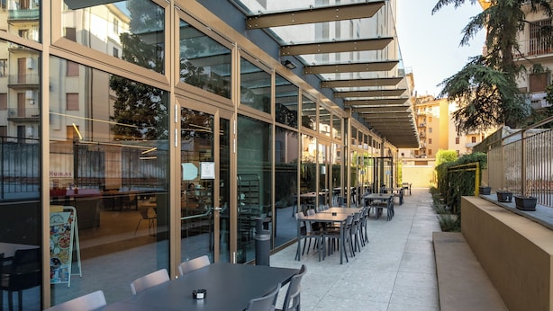 En udendørs café med borde, stole, store vinduer og en overdækket gang.