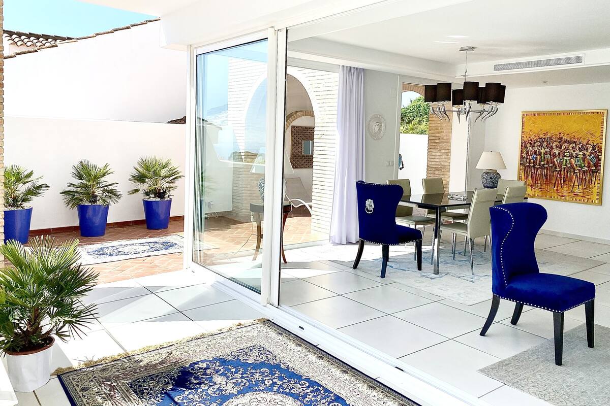 Una sala de estar moderna con un ventanal que da a un patio, una zona de comedor con mesa y sillas, y un cuadro grande en la pared.