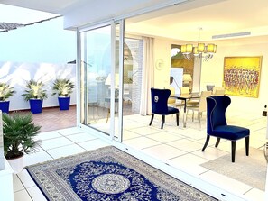 En rummelig opholdsstue med store glasdøre til en balkon, et spiseområde med moderne møbler og en dekorativ måtte.