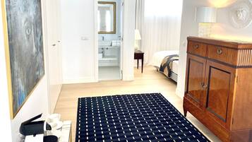 Habitación de hotel con un cuadro abstracto grande, un armario de madera, una cama con edredón estampado, un baño con espejo y lavabo, y vistas al exterior a través de una ventana.