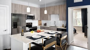Une cuisine moderne dotée d’un îlot central, d’appareils électroménagers en acier inoxydable et de luminaires suspendus.