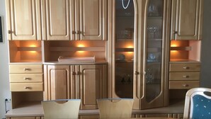 Een eetruimte met houten kasten, een glazen vitrine en een tafel met stoelen.