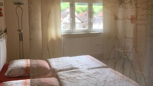 Een slaapkamer met een bed, een raam en een muur met een tekening.
