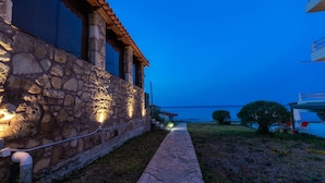 A stone building with a tiled roof, a stone pathway, and a view of the sea. - Georgia Apartments (Zakynthos)
