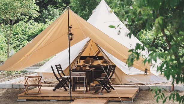 A tent with a dining table and chairs set up inside, surrounded by greenery. - Yoichi Vineyard Glamping (Yoichi)