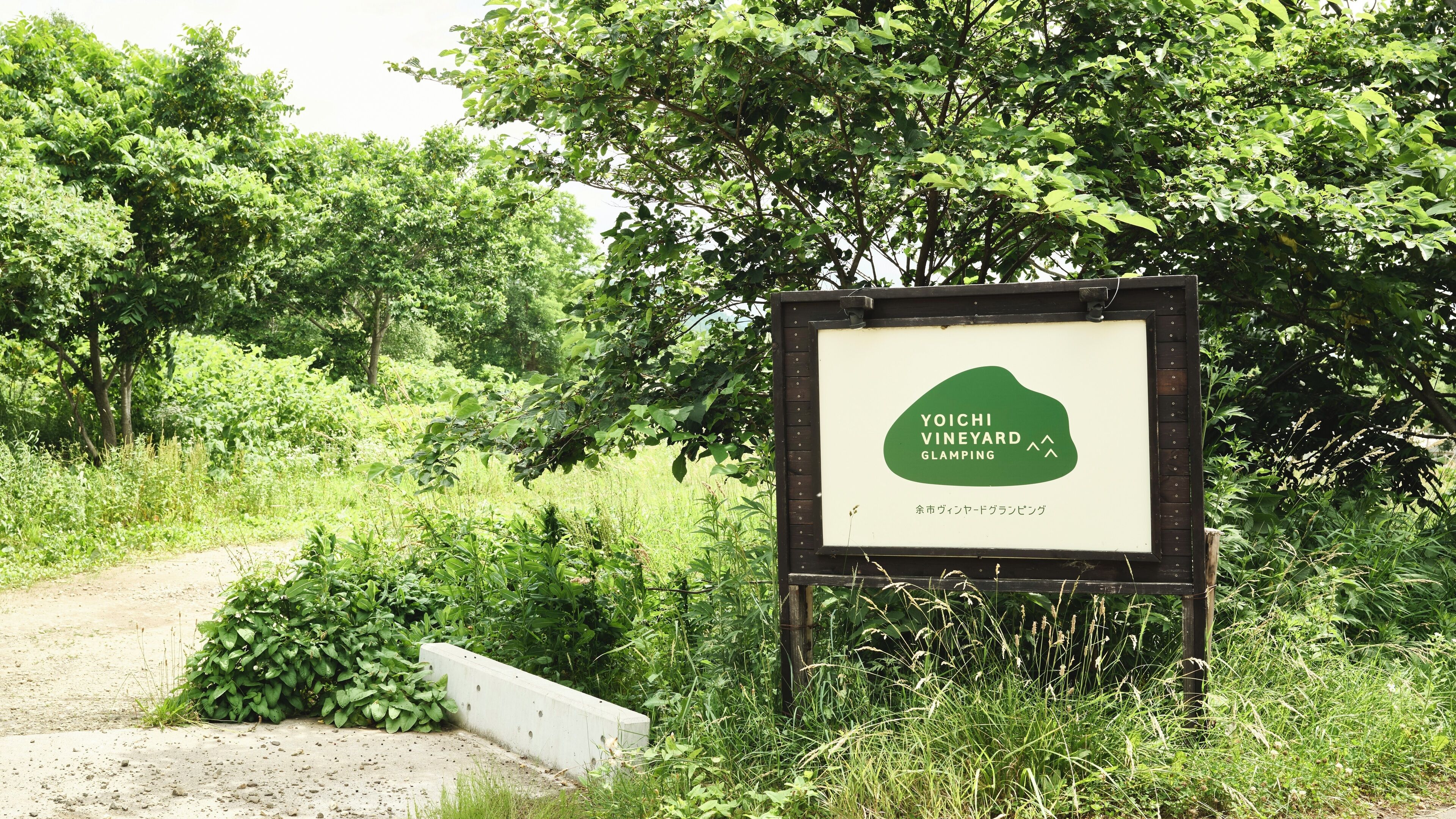 A sign for Yoichi Vineyard Glamping with a natural, green backdrop.