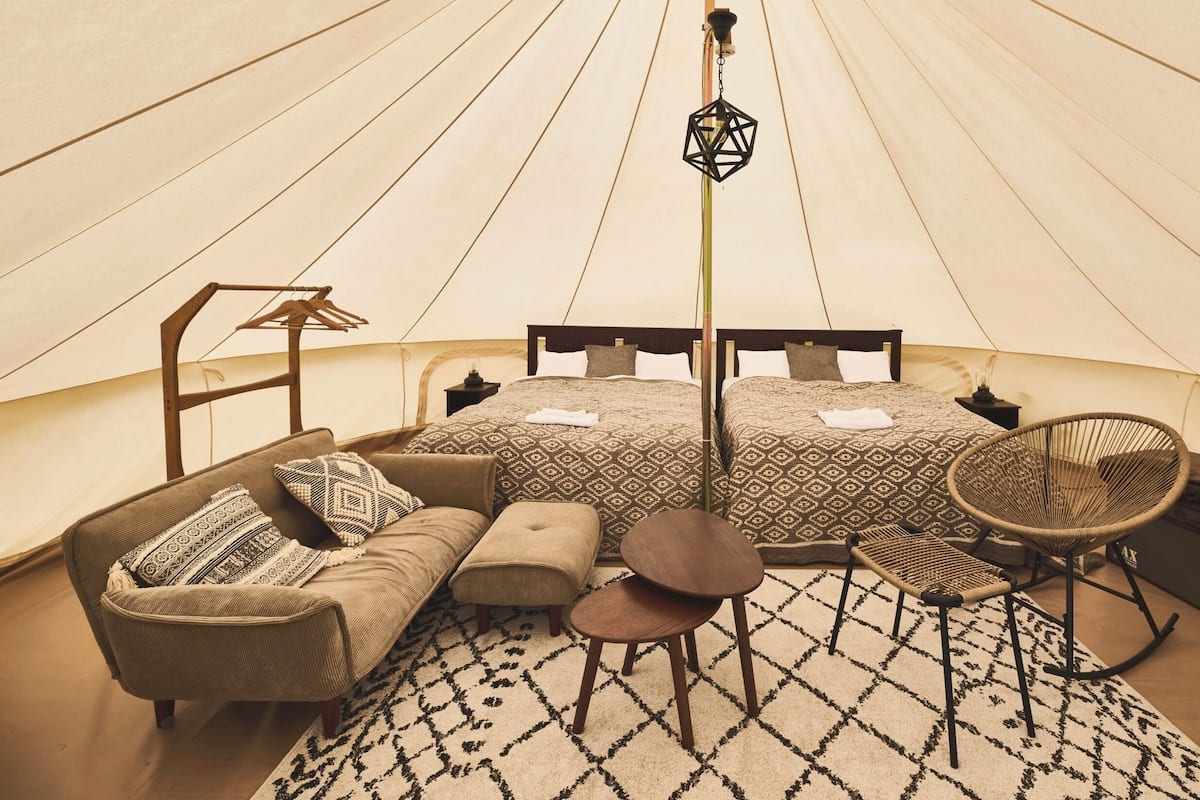 A tent-style room with two beds, a sofa, a chair, a small table, and a hanging light fixture.