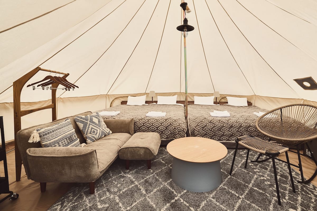 A tent with two beds, a sofa, a round table, and a chair.