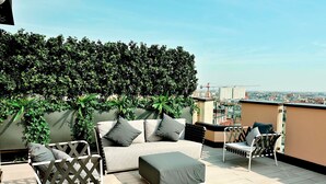 Eine Dachterrasse mit einer Couch, Stühlen und einem grünen Hecken.