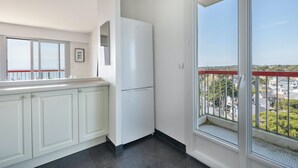 Una cocina moderna con armarios blancos, un refrigerador blanco y un ventanal con barandilla roja en el balcón.