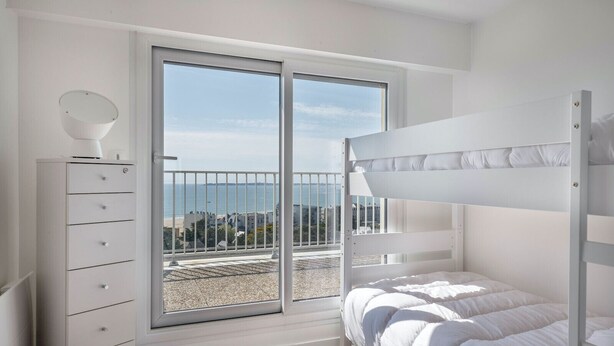 Un dormitorio con una cama litera, un aparador y un ventanal con vistas al mar.
