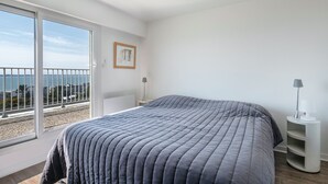 Un dormitorio con una cama grande, una mesita de noche, una lámpara y vistas al mar a través de una puerta corrediza de vidrio.