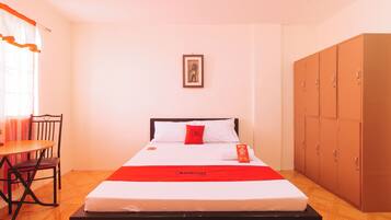 A hotel room with a bed, a chair, a desk, and a wardrobe.