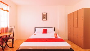 A hotel room with a bed, a desk, a chair, and a wardrobe. - Reddoorz @ FDB Homes Nueva Ecija (San Jose City)