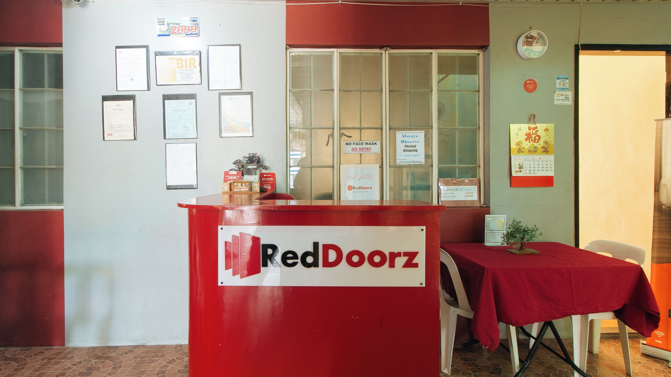 Un comptoir d’accueil RedDoorz avec des certificats encadrés accrochés au mur, une enseigne RedDoorz et un calendrier.