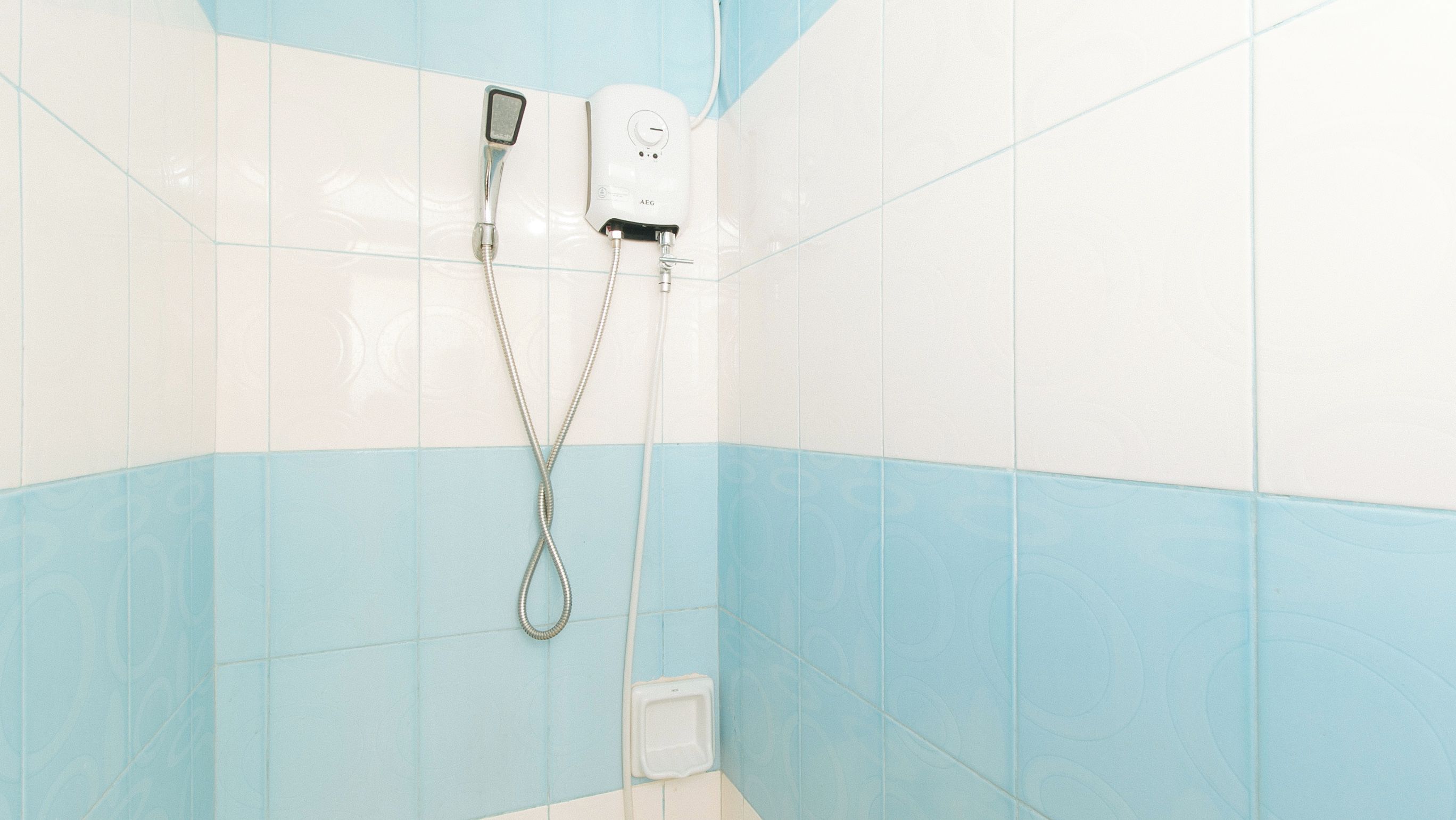 Un espace douche équipé d’un pommeau de douche à main et d’un panneau de commande fixé au mur.