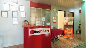 A RedDoorz reception desk with a red table and chairs, framed certificates on the wall, and a calendar. - Reddoorz @ FDB Homes Nueva Ecija (San Jose City)