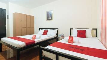 Two single beds with red bedspreads, a wooden wardrobe, and a framed picture on the wall.