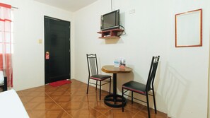 A small room with a black door, a television mounted on the wall, two chairs around a small round table, and a red doormat. - Reddoorz @ FDB Homes Nueva Ecija (San Jose City)