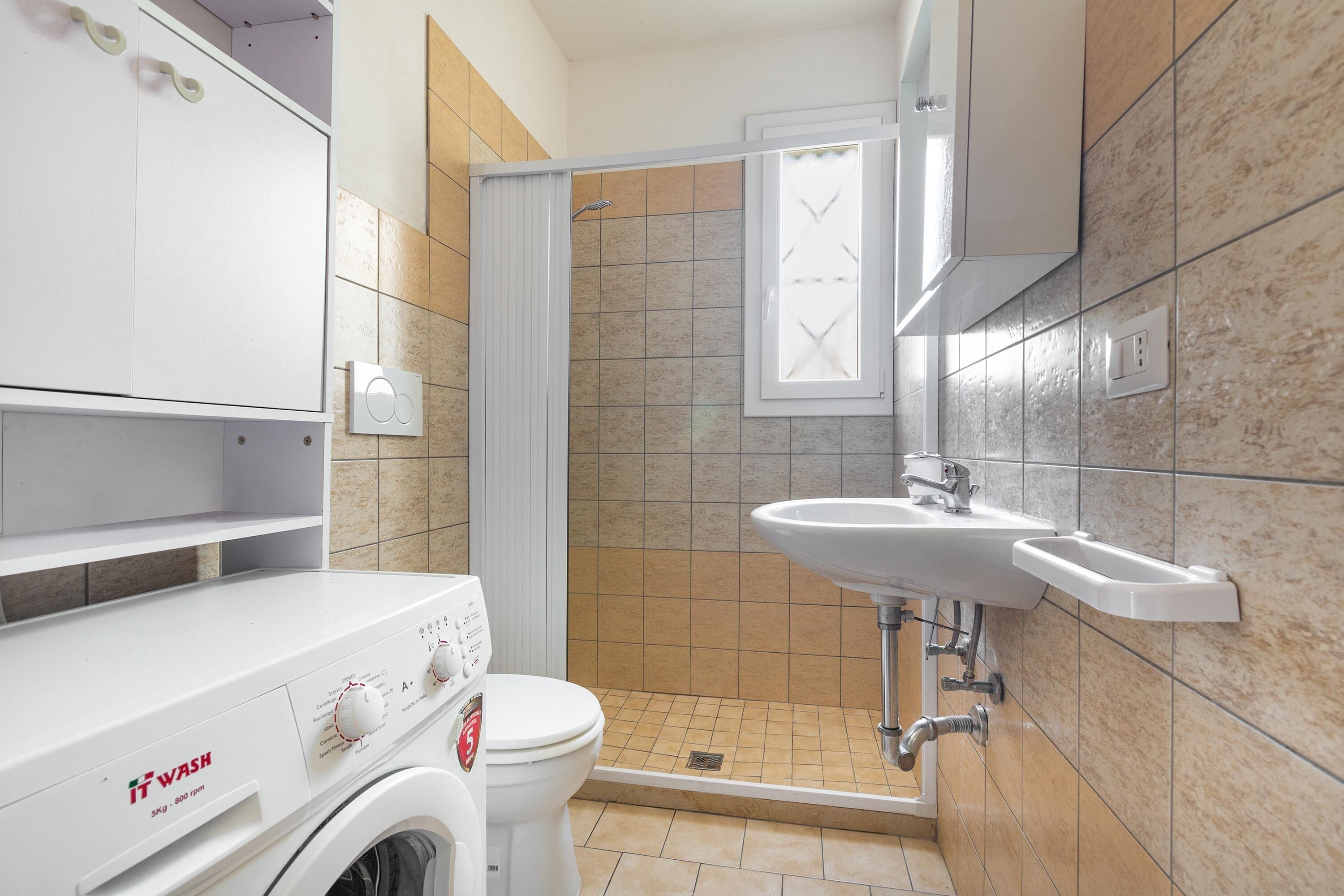 Un baño pequeño con lavadora, inodoro, zona de ducha y lavamanos.
