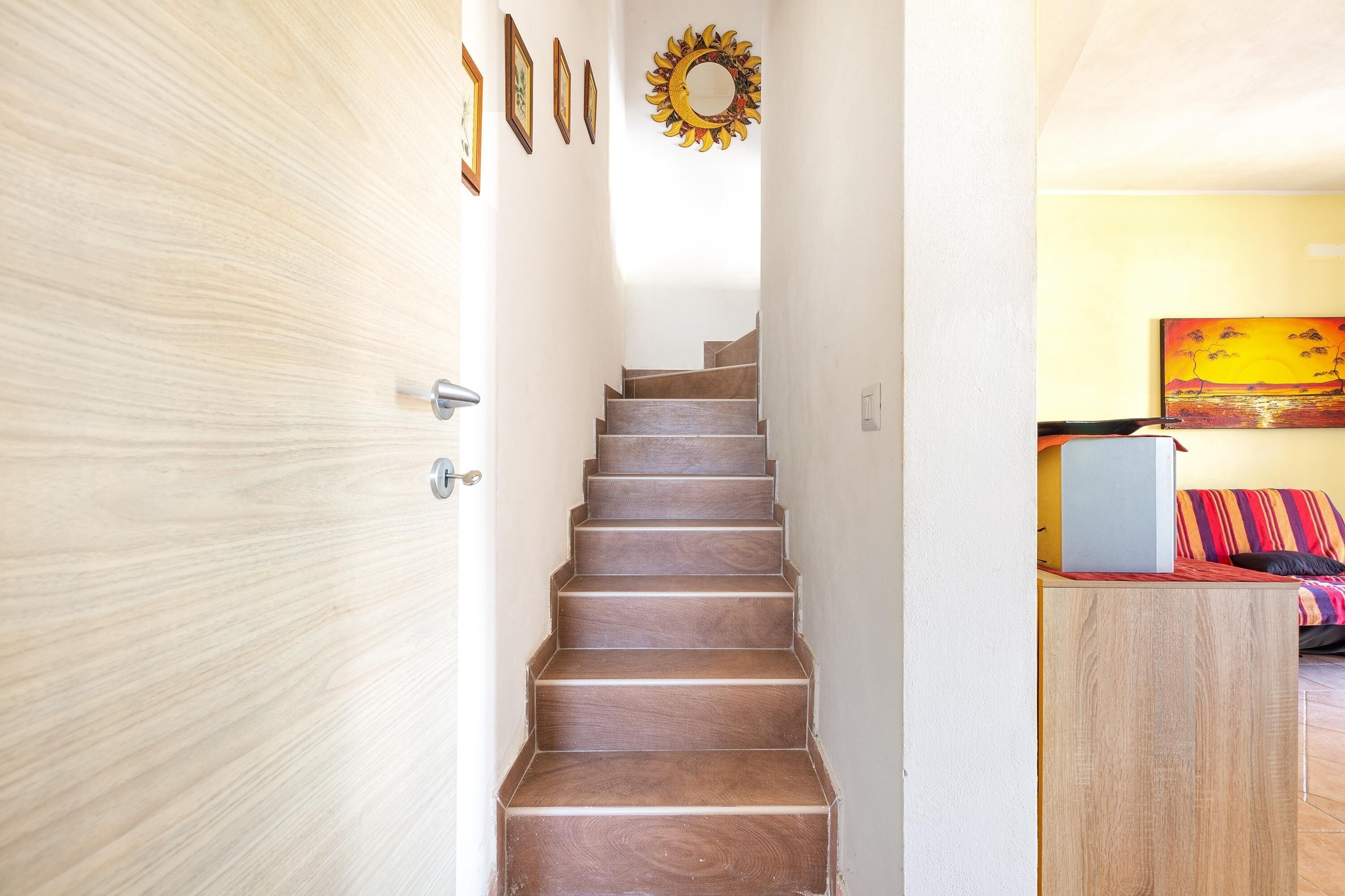 A wooden staircase leading to a room with a bed and a painting on the wall.